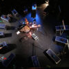 A stage from above. On it are boxes and objects arranged in a circle. In the middle, various instruments can be seen.