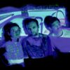Three young people stand close together in front of a blue projection that also lies over their faces.