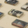 Auf einem hellen Holztisch liegen 8 alte Audiokassetten mit verschiedenen Covern, parallel zueinander angeordnet.