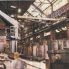 Ein altes Foto der ehemaligen Fabrikhalle, in der Kampnagel entstanden ist. Es stehen Kräne und große metallene Wannen auf Schienen unter einem schrägen, verglasten Dach.