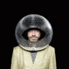 Jan Plewka, a white man with a short beard, wears a beige jacket with a striped shirt underneath. On his head he wears a large disco ball like a helmet, an oval lock is cut out of it, revealing his face.