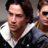 Close-up of Keanu Reeves and River Phoenix in their roles; Reeves wears a dark leather jacket, Phoenix looks over his shoulder, he wears dark sunglasses and a brown and red jacket.