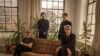 Band photo of Tocotronic: Four white slim men in black casual clothes in a room with large mullioned windows, white curtains and indoor plants. Two sit with crossed legs on a light brown leather sofa, two stand behind it.