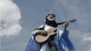 Alhousseini Anivolla steht mit einer Gitarre auf einem Hausdach. Im Hintergrund ist der Himmel zu sehen.