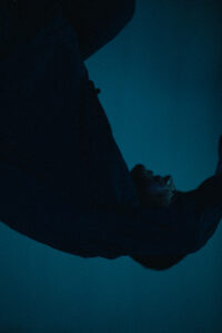 Abstrakt gedrehtes Bild eines Tänzers in gebogener Körperhaltung, in blaues Licht getaucht.