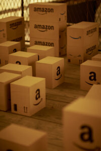 Various Amazon packages lie neatly on a wooden floor, some individually, some stacked. Inspired by the artwork "Brillo Box" by US artist Andy Warhol.