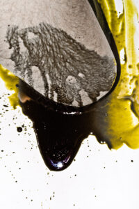 A hairy white knee lying in a pool of yellow and black paint, partially covered by black paint flowing down.