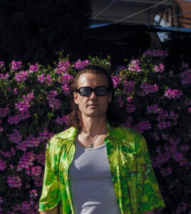 Der Künstler in einem knall grünen Hemd vor einem Blumenbusch