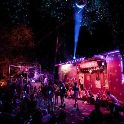 Party vor dem Migrantpolitan. Besucher*innen bewegen sich in pinkem Licht unter einer Discokugel.