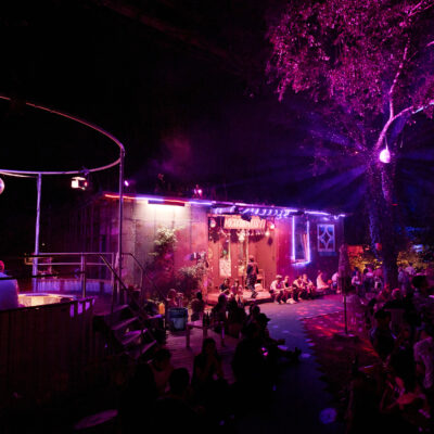 Feierliche Stimmung beim Migrantpolitan. Das Gebäude ist in pinkem Licht angeleuchtet, über dem Pool hängt eine Discokugel.