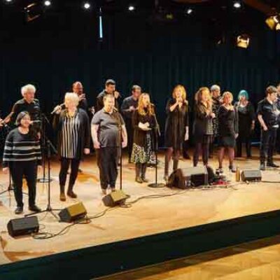 Eine Gruppe von Menschen steht auf einer Bühne und singt gemeinsam in Mikrofone.