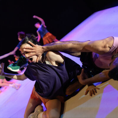 Two performers in Ayelen Parolin’s production “Irresistible Revolution” interact on stage. One person holds the  hand in front of the other’s face.