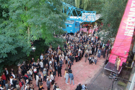 Ein Foto von Oben mit Blick auf eine kleine Bühne und eine Menschenmenge, draußen auf dem Kampnagelgelände.
