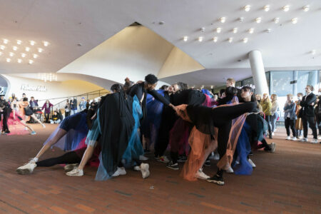 Ca. 40 Tänzer*innen sind ganz dicht beieinander in einer großen Gruppe auf der Elbphilharmonie Plaza. Sie tragen schwarze Kostüme mit bunten Tülltüchern.