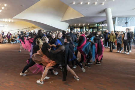 Ca. 40 Tänzer*innen sind ganz dicht beieinander in einer großen Gruppe auf der Elbphilharmonie Plaza. Sie tragen schwarze Kostüme mit bunten Tülltüchern.