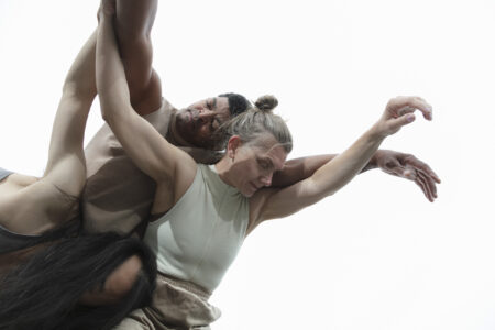 Three people are nestled close together against a white background. Their bodies and arms are close together and intertwined in a falling motion