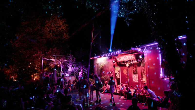 Party vor dem Migrantpolitan. Besucher*innen bewegen sich in pinkem Licht unter einer Discokugel.