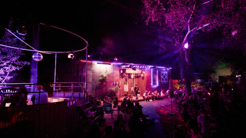 Feierliche Stimmung beim Migrantpolitan. Das Gebäude ist in pinkem Licht angeleuchtet, über dem Pool hängt eine Discokugel.